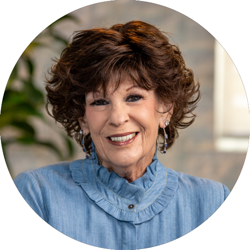 Elderly female patient with brown hair smiling and a blue blouse, showing her all-on-4 dental implants.