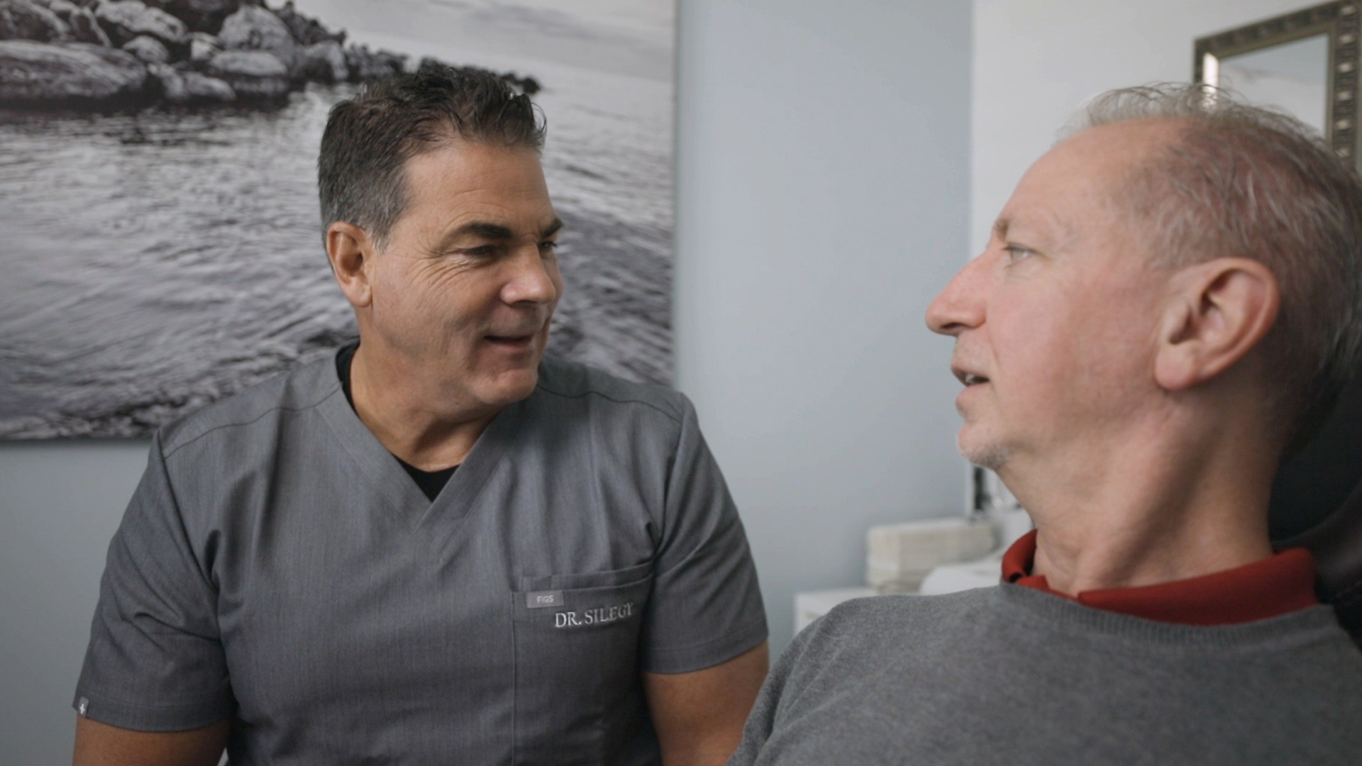 Dr. Silegy talking with middle-aged male all-on-4 dental implant recipient in exam room.