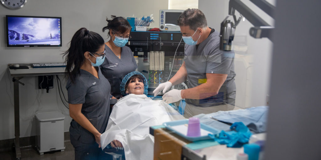 Dr. Silegy wearing scrubs in operatory with elderly female patient receiving all-on-4 dental implants.